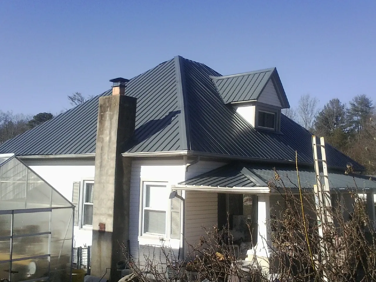 Dark blue standing seam metal roof on a white farmhouse with dormer — Slate & Tile Roof Repair by Roofing Brothers in Fort Drum