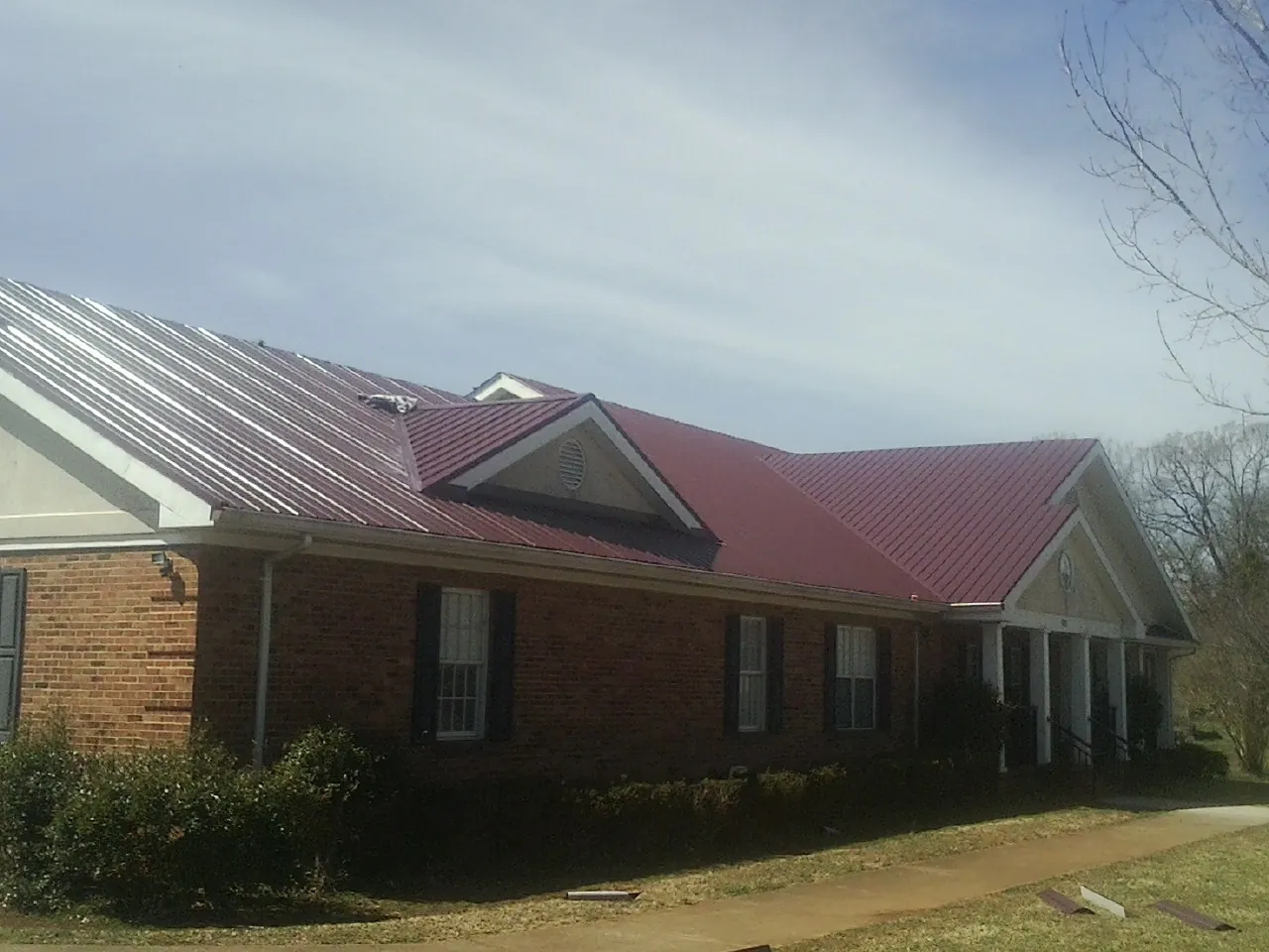 Red metal roof with gabled entries on a long brick building, from a Hail Damage Roof Repair job in Fort Drum