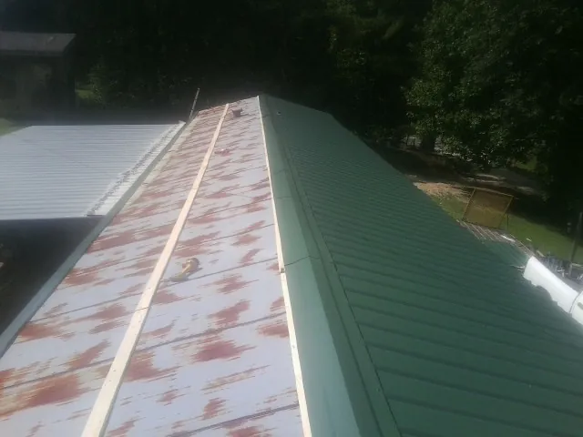 Old rusted panels beside newly installed green metal roofing — Wind Damage Roof Repair by Roofing Brothers in Fort Drum