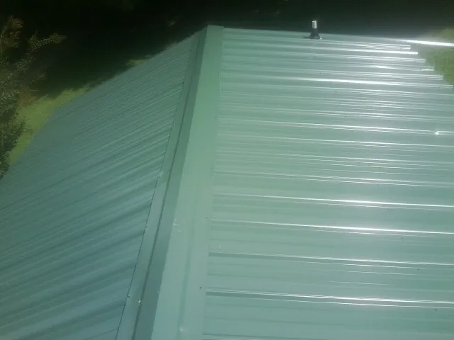 New green metal panels meeting at the ridge of a roof — Flat Roof Repair work by our crew in Fort Drum