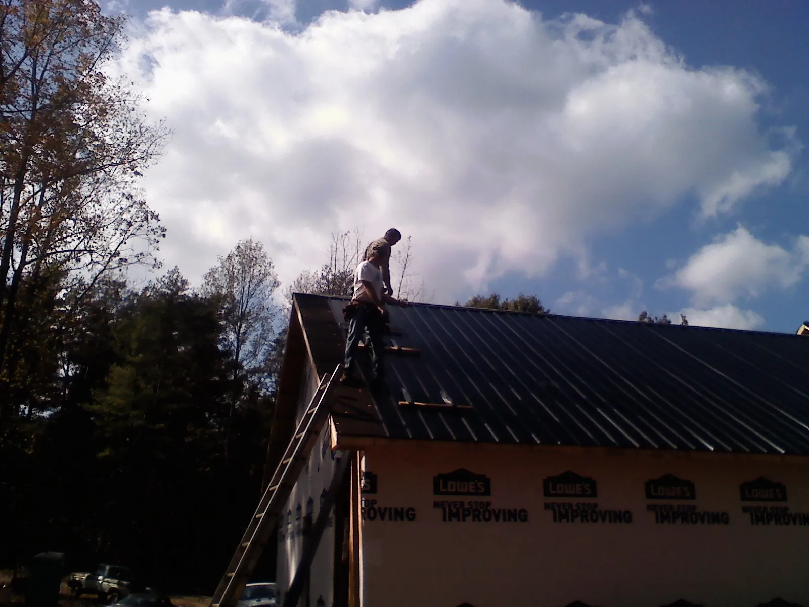 Roofer fastening dark metal panels high against a cloudy sky, from a Roof Inspection job in Fort Drum