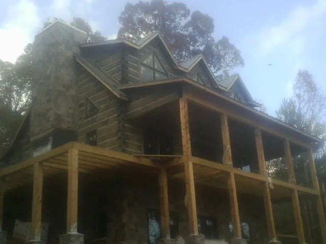 Stone chimney and dormers on a large log home with a timber porch in Fort Drum