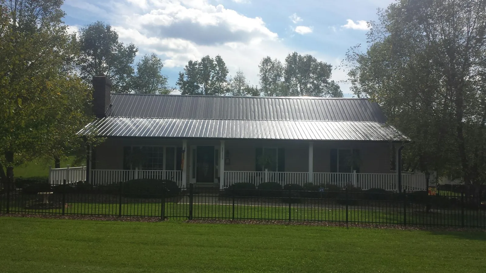 Gray metal roof on a brick ranch with a full width front porch — Gutter Guard Installation work by our crew in Fort Drum