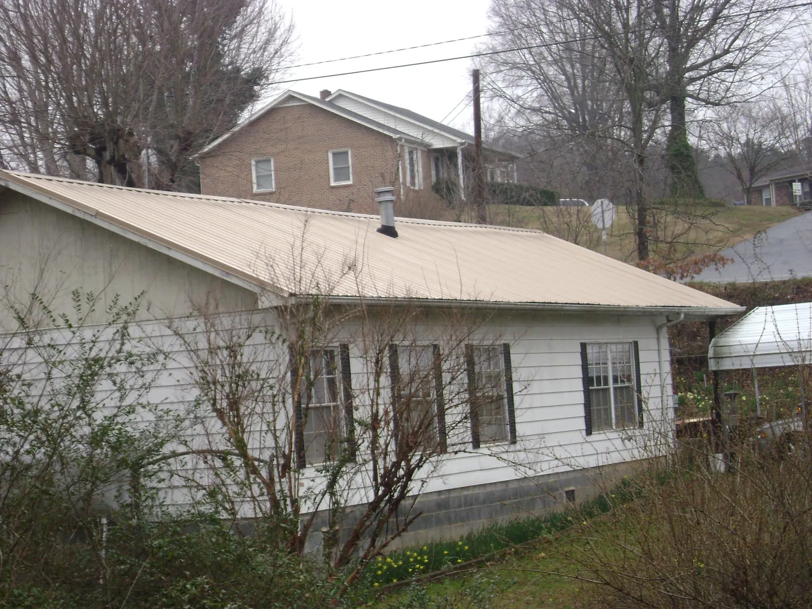 Tan metal roof on a white sided house set into a hillside — Commercial Roofing by Roofing Brothers in Fort Drum