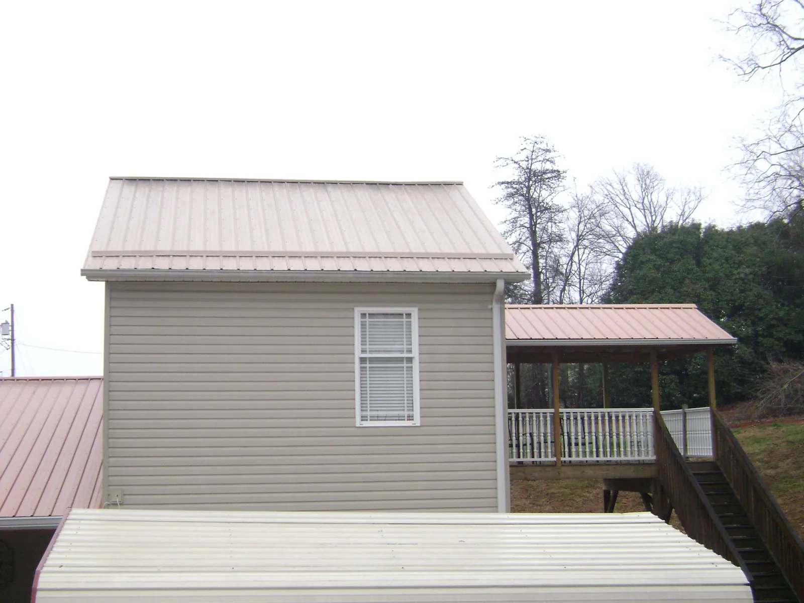 Tan metal roofs on a two story addition and attached porch, from a Roof Replacement job in Fort Drum