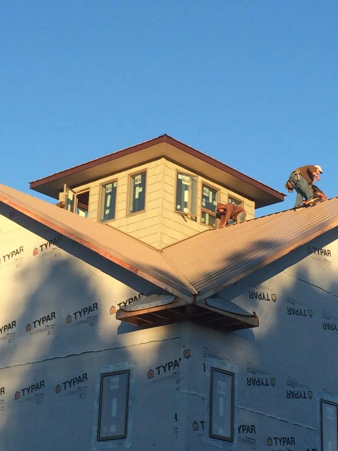 Roofers working around a rooftop cupola on a new metal roof at sunset — Roof Waterproofing in Fort Drum by Roofing Brothers